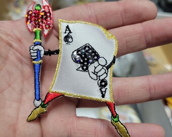 May include: Embroidered Ace of Spades patch with a cartoon design. The card has a gold border, black arms, and red and gold shoes. It holds a red and green axe with a blue and gold handle.