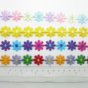 May include: Five rows of colorful daisy flower trim with white centers. The trim is shown on a white surface with a ruler for scale.