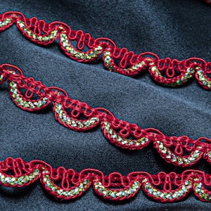 May include: Close-up of decorative red trim with a scalloped edge. The trim features a gold and iridescent sequin detail within each scallop. The trim is set against a dark blue fabric background, creating a contrast.