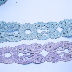 Peut inclure: Deux galons décoratifs, l'un bleu clair et l'autre lavande, avec un motif floral et des détails découpés.