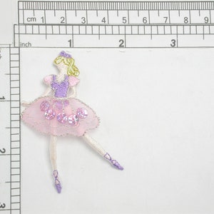 May include: A pink and purple ballerina applique with a sequined skirt and blonde hair. The applique is approximately 4 cm tall.