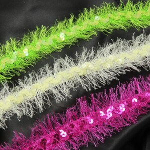 May include: Three trims of fringe with sequins. The trims are green, white, and pink.