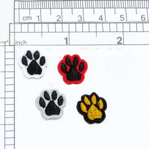 May include: Four iron-on patches in the shape of a paw print. The patches are white with black paw prints, red with black paw prints, gray with black paw prints, and yellow with black paw prints.