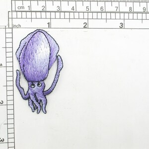 May include: Purple embroidered iron-on patch of a cartoon squid with large eyes and eight tentacles.