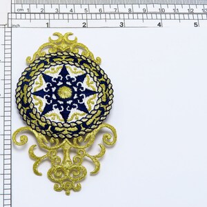 May include: Gold and blue embroidered patch with a star design. The patch is about 5 inches in diameter and has a decorative border.