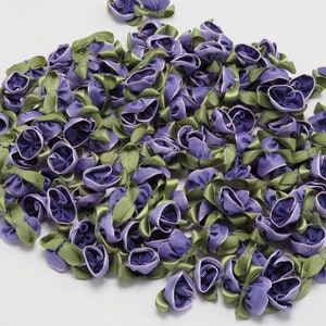 May include: A large pile of purple and green satin ribbon flowers. The flowers are about 1 inch in diameter and have a ruffled appearance.