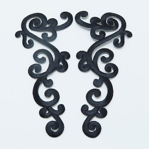 May include: Two black fabric appliques with a decorative scroll design. The appliques are symmetrical and have a delicate, intricate pattern.