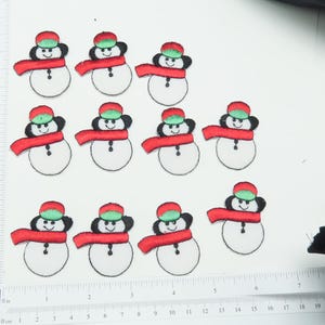 Könnte beinhalten: Zehn rote und grüne Filz-Schneemann-Applikationen mit weißen Gesichtern und schwarzen Augen. Die Schneemänner tragen rote Schals und grüne Hüte.