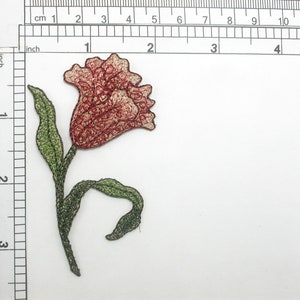 Pode incluir: Remendo de flor bordada com uma flor vermelha e dourada, caule e folhas verdes. O remendo mede aproximadamente 5 cm de altura e 2,5 cm de largura. A flor é um elemento decorativo detalhado.