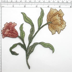 Pode incluir: Aplique bordado com duas flores e folhas verdes. As flores são rosa claro e castanho claro.