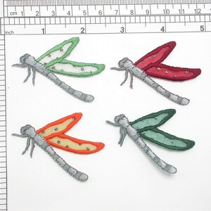 May include: Four iron-on dragonfly patches in various colors: green, red, orange, and blue. Each patch has a silver-gray body and wings with a glittery finish.