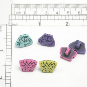 May include: A collection of colourful, miniature shirt-shaped buttons. The buttons are in various colours, including teal, purple, pink, and yellow, with black decorative details. The buttons are approximately 2 cm in length.