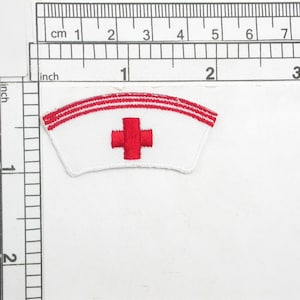 May include: White embroidered patch with a red cross and three red stripes. The patch is shaped like a nurse's cap.