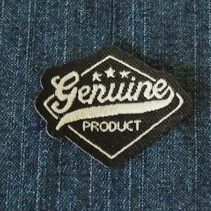 May include: Black and white embroidered patch in a diamond shape. The patch reads "Genuine Product" with three stars above the word "Genuine".