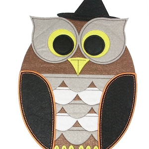 Könnte beinhalten: Eine braune und graue Filzeule mit einem schwarzen Hexenhut. Die Eule hat gelbe Augen und einen gelben Schnabel. Die Flügel der Eule sind schwarz und der Körper ist mit einem Muster aus Braun, Grau und Weiß verziert.