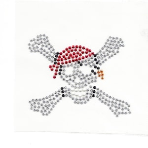 May include: A silver, red, and black skull and crossbones design made of rhinestones. The skull is wearing a red bandana.