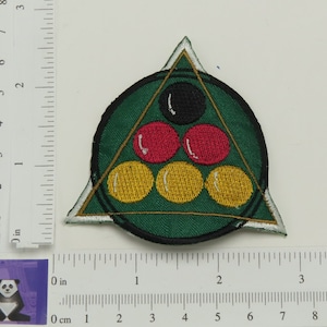 May include: A green felt triangle with a white outline and a circle inside. The circle contains five billiard balls: a black ball, two red balls, and two yellow balls. The balls are arranged in a pyramid shape.