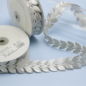 May include: Silver leaf trim ribbon on a white spool. The ribbon is 6 meters long and has a silver leaf design.
