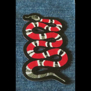 May include: A red and black embroidered snake patch. The snake is coiled and has white stripes.