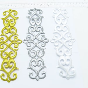 May include: Three embroidered trim pieces with a decorative heart design. The trim pieces are gold, silver, and white.