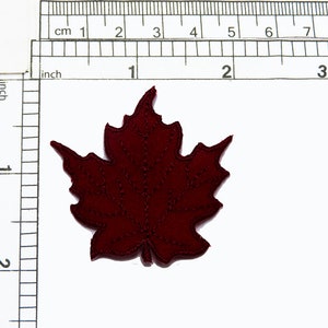 May include: A dark red felt maple leaf applique, approximately 5 cm wide.