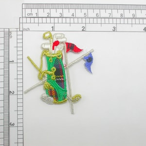 Puede incluir: Parche bordado con una bolsa de golf con palos, una bandera roja y azul y un contorno dorado. La bolsa de golf es verde con un estampado de cuadros. El parche mide aproximadamente 5 cm de altura.