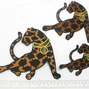 Pode incluir: Três patches de ferro bordados de leopardos pretos e castanhos que usam colares dourados. Os leopardos estão em poses diferentes.
