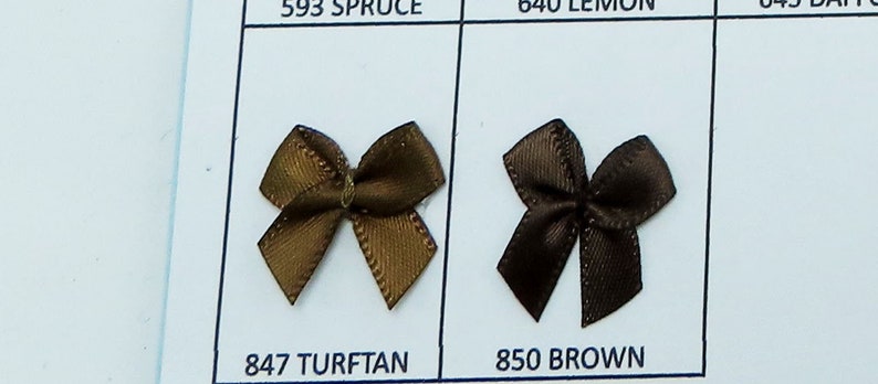 May include: Two brown satin bows, one a lighter brown with a gold sheen and the other a darker brown. The bows are labeled "847 TURFTAN" and "850 BROWN".