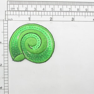 May include: A bright green sequined seashell patch. The patch is approximately 2 inches in diameter and features a spiral design. The sequins are a vibrant green color, and the patch has a black border.
