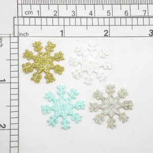 May include: Four snowflake-shaped fabric patches in different colors: gold, white, light blue, and silver. The patches are arranged in a square pattern on a white background.