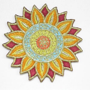 May include: A colorful embroidered patch in the shape of a sun with a gold, yellow, orange, red, and blue design.