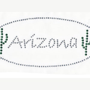 May include: A white oval with a silver rhinestone border and the word "Arizona" in silver rhinestones. Two green cactus silhouettes are on either side of the word.
