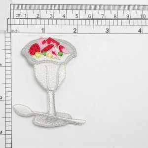 Può includere: Toppa ricamata bianca da stirare di un parfait con un cucchiaio. Il parfait è riempito con frutta rossa e bianca e ricoperto di panna montata.