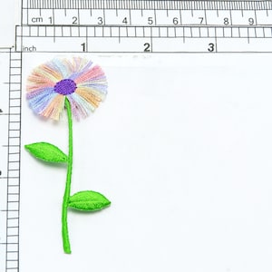 Può includere: Un ricamo di un fiore colorato con un centro arcobaleno e foglie verdi. Il fiore ha un diametro di circa 5 cm.