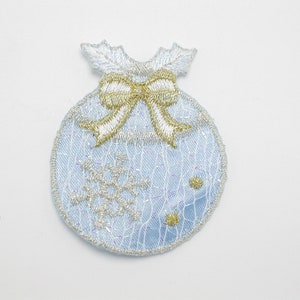 Może przedstawiać: Niebieska ozdoba choinkowa z złotą kokardką i wzorem płatka śniegu. Ozdoba jest wykonana z tkaniny i ma błyszczące wykończenie.