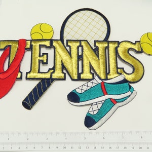 以下が含まれることがあります： 「TENNIS」という文字が大きく刺繍された金色のパッチ。パッチには、テニスラケット、テニスボール2個、テニスシューズ1足も描かれている。