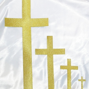 May include: Four gold glitter crosses of different sizes on a white background. The crosses are arranged in a descending order of size from left to right.