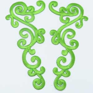 May include: Two green embroidered fabric appliques with a floral design. The appliques are shaped like a vine with swirls and loops.