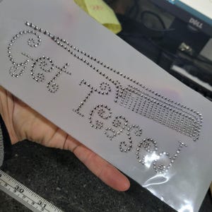 May include: A sheet of silver rhinestones spelling out "Get Blessed" in a cursive font. The design includes a cross and a decorative element. The rhinestones are set on a light gray backing.