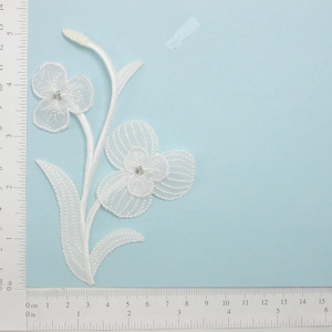May include: White lace flower applique with a beaded stem and two flowers. The larger flower has a rhinestone center. The applique measures approximately 6 inches in length.
