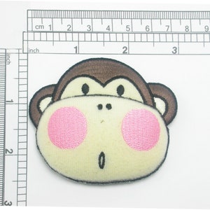 May include: Embroidered monkey face patch with brown, cream, and pink details. The patch is approximately 7.6 cm wide. Features a surprised expression with pink cheeks and a small open mouth. Suitable for clothing or accessories.