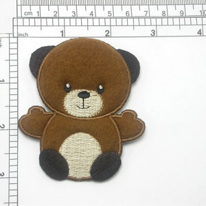 Könnte beinhalten: Braunes Filz-Teddybär-Applikationsmotiv mit schwarzen Augen, Nase und Füßen. Der Bär hat einen weißen Bauch und ein gesticktes Lächeln.