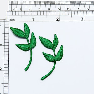 May include: Two green embroidered fabric leaf sprigs, each with three leaves, on a white background.