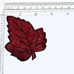 May include: A burgundy felt leaf applique with a detailed embroidered vein pattern. The leaf is approximately 3 inches in length.