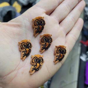 May include: Five embroidered owl patches. Each patch features a detailed design with orange and black thread, showcasing the owl's features. The patches are small, suitable for embellishing clothing or accessories.