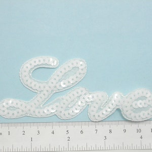 May include: White sequined fabric applique in the shape of the word "Love".