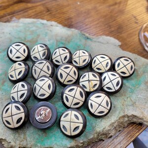 May include: A collection of 16 black and white round buttons with a carved design. The buttons have a raised white design on a black background.