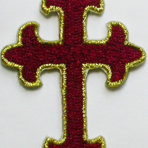 Könnte beinhalten: Ein kastanienbraunes Kreuz mit goldener Umrandung. Das Kreuz hat eine traditionelle Form mit vier Armen und einer spitzen Oberseite.