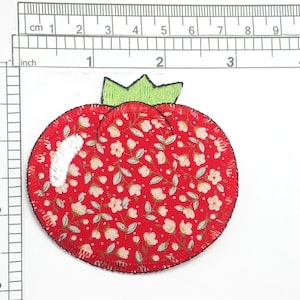 May include: Red fabric tomato with a green stem and white floral pattern. The tomato is approximately 2 inches in diameter.