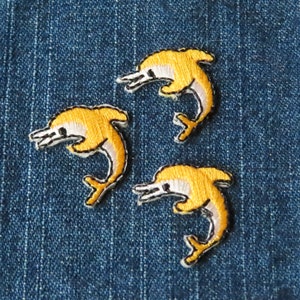 May include: Three embroidered yellow dolphin patches on a blue denim background.